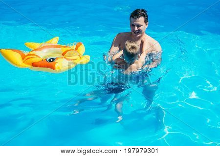 Father and his son having fun in the swimming pool on beautiful summer day.