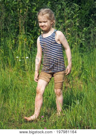Dirty happy child is on the grass. Bright sun summer heat. Girl in the sand