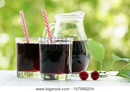 Two glasses of cherry juice with jar on a green background