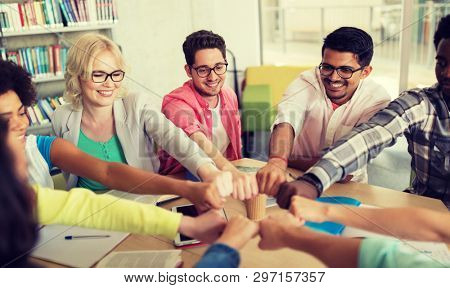 education, school, teamwork and people concept - group of international students sitting at table and making fist bump