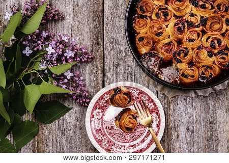 Homemade Mini Cherry Rolls In A Baking Form And Two Rolls On A Plate With Bouquet Of Lilac On Vintag