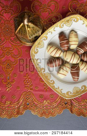 Chocolate coated dates served in a decorative plate- an Arabic sweet or dessert. Delicious date- chocolates and Ramdan lamp shot from above.