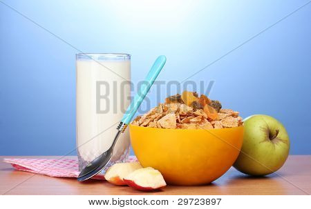 leckere Cornflakes in gelbe Schale, Äpfel und Glas Milch auf Holztisch auf blauem Hintergrund