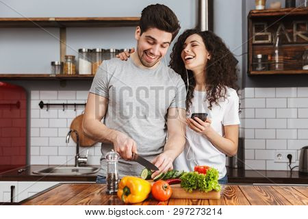 Portrait of happy couple man and woman 30s listening to music together while cooking salat in kitchen at home