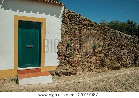 Closed Door In A Plaster White Wall Next To A Stone And Bricks Wall In Sunny Day, From A Street Of E