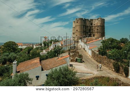 People Walking Up The Main Cobblestone Street In A Sunny Day Towards The Castle Of Evoramonte. A Tin