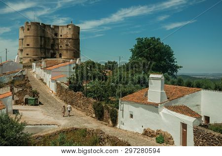 People Walking Up The Main Cobblestone Street In A Sunny Day Towards The Castle Of Evoramonte. A Tin