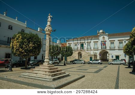 Marble Pillory With Sculpture In Square, Old Buildings And City Hall In The Back, In A Sunny Day At 