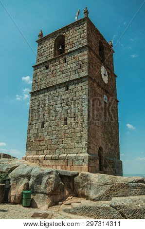 Charming facade of old stone tower with bell and clock over rocky hilltop in a sunny day at Monsanto. Considered one of the cutest and most peculiar historic village of Portugal.