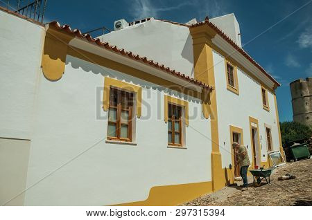 Evoramonte, Portugal - July 6, 2018. Mason working in front of colorful house at the main street of Evoramonte. A tiny fortified civil parish over hill where stands out its historic castle in Portugal