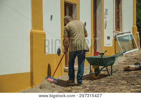 Evoramonte, Portugal - July 6, 2018. Mason working in front of colorful house at the main street of Evoramonte. A tiny fortified civil parish over hill where stands out its historic castle in Portugal