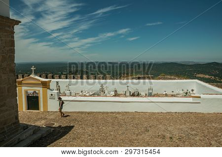 Evoramonte, Portugal - July 6, 2018. Woman walking in front of cemetery, in the main street of Evoramonte. A tiny fortified civil parish over hill where stands out its historic castle in Portugal.