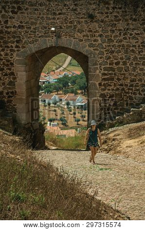 Evoramonte, Portugal - July 06, 2018. Woman walking through gateway on stone wall, in street of Evoramonte. A tiny fortified civil parish over hill where stands out its historic castle in Portugal.