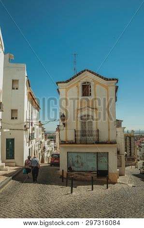 Elvas, Portugal - July 07, 2018. Street with colorful old houses in a narrow causeway and elders walking at Elvas. A gracious star-shaped fortress city on the easternmost frontier of Portugal.