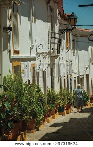 Elvas, Portugal - July 7, 2018. Old colorful houses with vases and old woman walking in an alley on sunny day at Elvas. A gracious star-shaped fortress city on the easternmost frontier of Portugal.