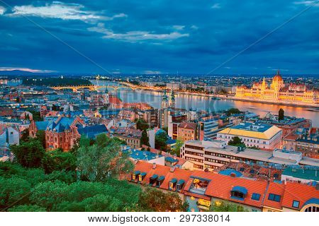 View Of Illuminated Parlament And Riverside Of Danube River In Budapest, Hungary During Sunset With 