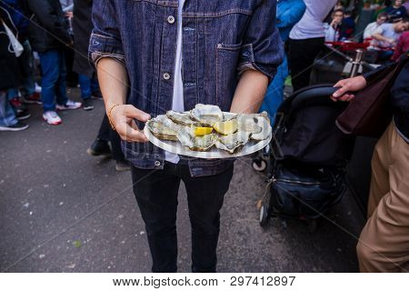 Man Hand Holding Fresh Raw Oyster In Paperr Plate With Lemon In Market.