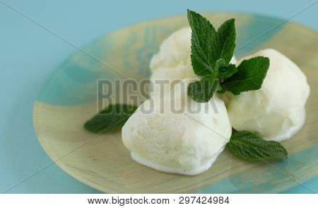 Close-up Of Three Vanilla Ice Cream Balls With Mint On A Blue-beige Plate With A Blue Background