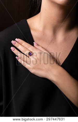 Womens Gold Ring With Purple Stone In The Middle In The Shape Of A Square On The Finger, On A Black 