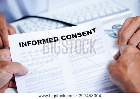 closeup of a senior caucasian man, at the doctors office, reading an informed consent document in front of a caucasian doctor man, in a white coat, sitting both at the doctors desk