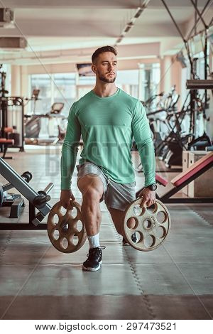 Sportive Attractive Man In Green Training Shirt Is Doing His Exsercises In Gym With Weights.