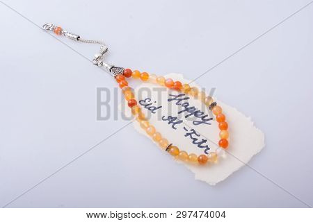 The Word Eid El Fitr  Written On Torn Paper Beside Prying Beads