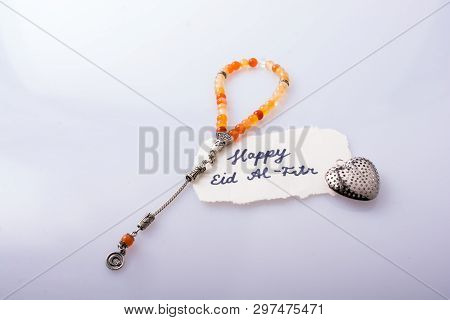 The Word Eid El Fitr  Written On Torn Paper Beside Prying Beads