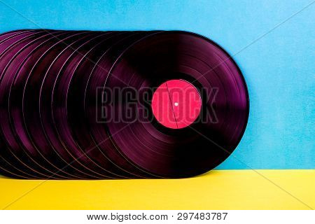 Many Black And Pink Colored Vinyl Discks Placed  In A  Line On Yellow And Blue Background.