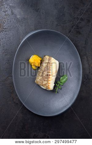 Fried Danish skrei cod fish filet with wasabi lettuce and lemon curd as top view on a modern design plate with copy space 