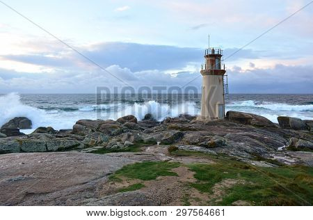 Old Lighthouse And Waves Breaking Against The Rocks With Sunset Light. Muxia, Spain.