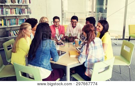 education, high school, learning, people and technology concept - group of international students sitting at table with tablet pc computers and books and talking at university