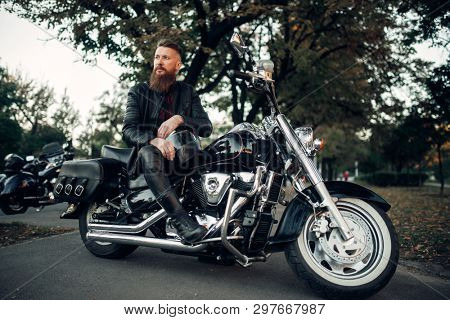 Baerded biker poses on chopper leaning on a helmet