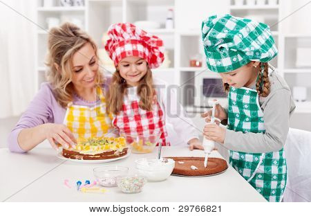 Woman and her daughters in the kitchen making a cake together