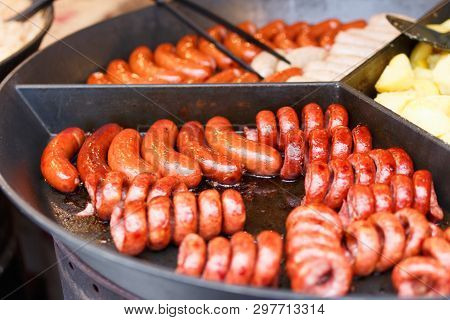 Close Up Image A Lot Of Tasty Pork Sausages And Other Meat Cooking On A Round Flat Grill. Fried Back