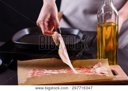 Young Woman In A Gray Apron Fries Bacon