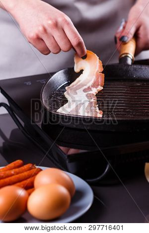 Young Woman In A Gray Apron Fries Bacon