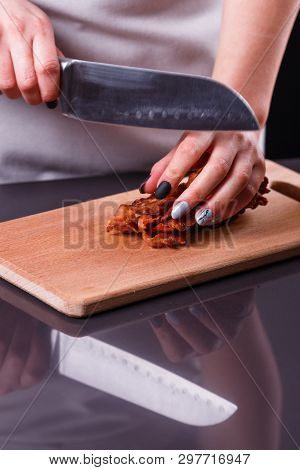 Young Woman In A Gray Apron Cuts Roasted Bacon