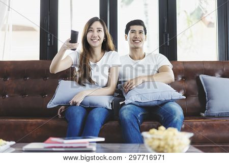 Happy Asian Young Couple Loving On The Couch Watching A Movie Together, Woman Holding Remote And Her