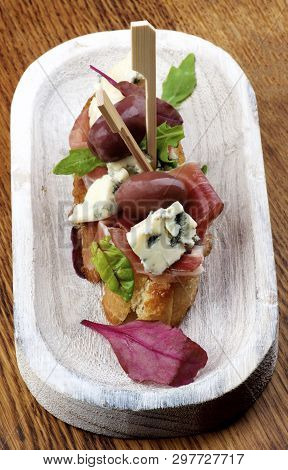 Delicious Spanish Tapas With Rochefort Cheese, Jamon And Red Olives With Greens Closeup On White Woo