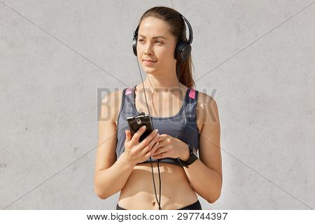 Portrait Of Attractive Sporty Woman In Sportive Bra Listening To Music With Earphones And Smartphone