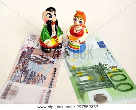 Figurines In The Ukrainian National Suits Stand On Paper Russian And Euro Banknotes. Ukraine At The 