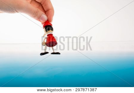 Hand Holding Wodden Puppet Pinocchio On In Blue Water