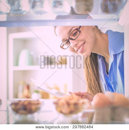 Portrait Of Female Standing Near Open Fridge Full Of Healthy Food, Vegetables And Fruits. Portrait O