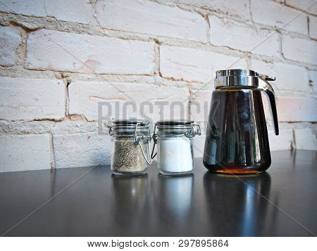 Salt And Pepper Shakers And Syrup Dispenser With Reflection On Cafe Table Next To A Painted Brick Wa