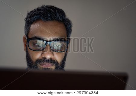 Mature businessman wearing eyeglasses while using laptop in a dark office. Middle eastern man working late at office. Overworked man with specs in front of laptop with copy space.