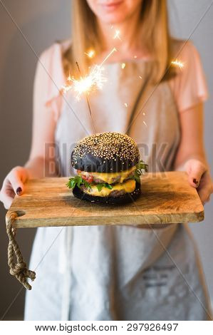 Girl Chef Holds In Her Hands A Wooden Cutting Board With A Black Cheesburgers.