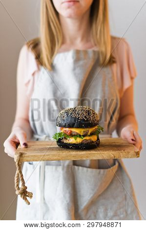 Girl Chef Holds In Her Hands A Wooden Cutting Board With A Black Cheesburgers.