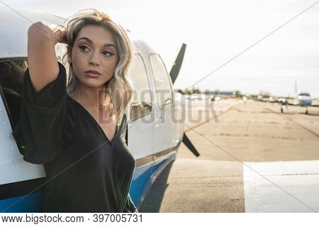 A gorgeous young blonde model poses outdoors with a single engine aircraft at a local airport