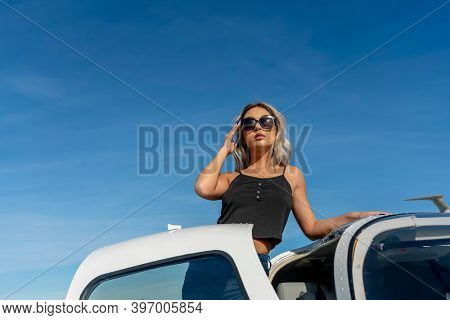 A gorgeous young blonde model poses outdoors with a single engine aircraft at a local airport