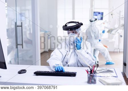 Dentist Nurse In Ppe Suit Discussing With Patient On The Phone During Covid19. Medicine Team Wearing